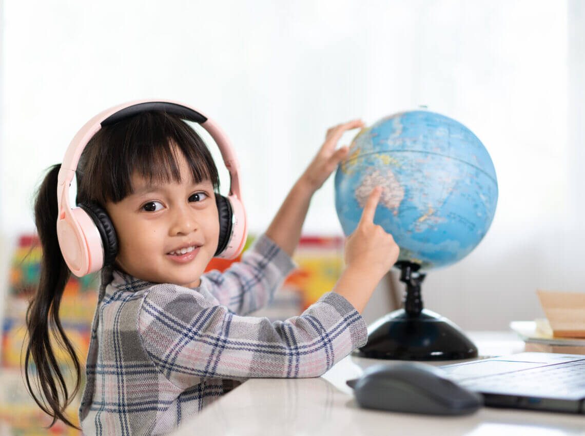 Asian beautiful little student girl is pointing on bilingual globe model for online lesson.